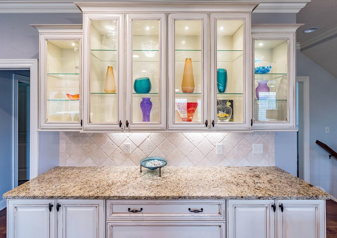 Honey-toned granite counter under lit glass cabinets